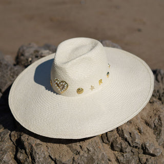 El Sombrero Panamá Charlotte es una pieza diseñada para destacar. Su ala ancha y su silueta estructurada crean una presencia sofisticada y muy favorecedora, mientras que los delicados apliques dorados aportan un toque distintivo que eleva cualquier look con naturalidad.